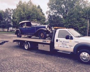 A tow truck transporting an old car, showcasing the vehicle secured on its flatbed for safe transport.