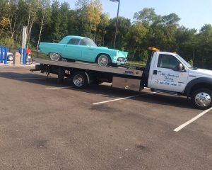 A tow truck transporting a blue car on its flatbed, showcasing the vehicle's secure placement for safe transport.