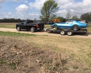 A blue car is being towed by a truck on a road, showcasing the towing process in action.