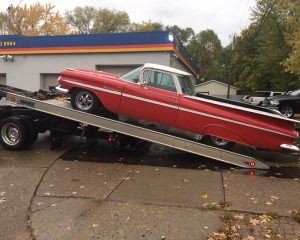 A red car is being towed on a flatbed tow truck, showcasing the vehicle's vibrant color against the truck's neutral tones.