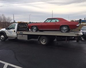 A tow truck transporting a red car on its flatbed, showcasing the vehicle's sleek design against a clear background.