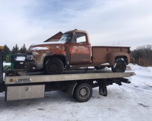 An old truck is being towed by a flatbed truck on a clear day, showcasing the contrast between the two vehicles.